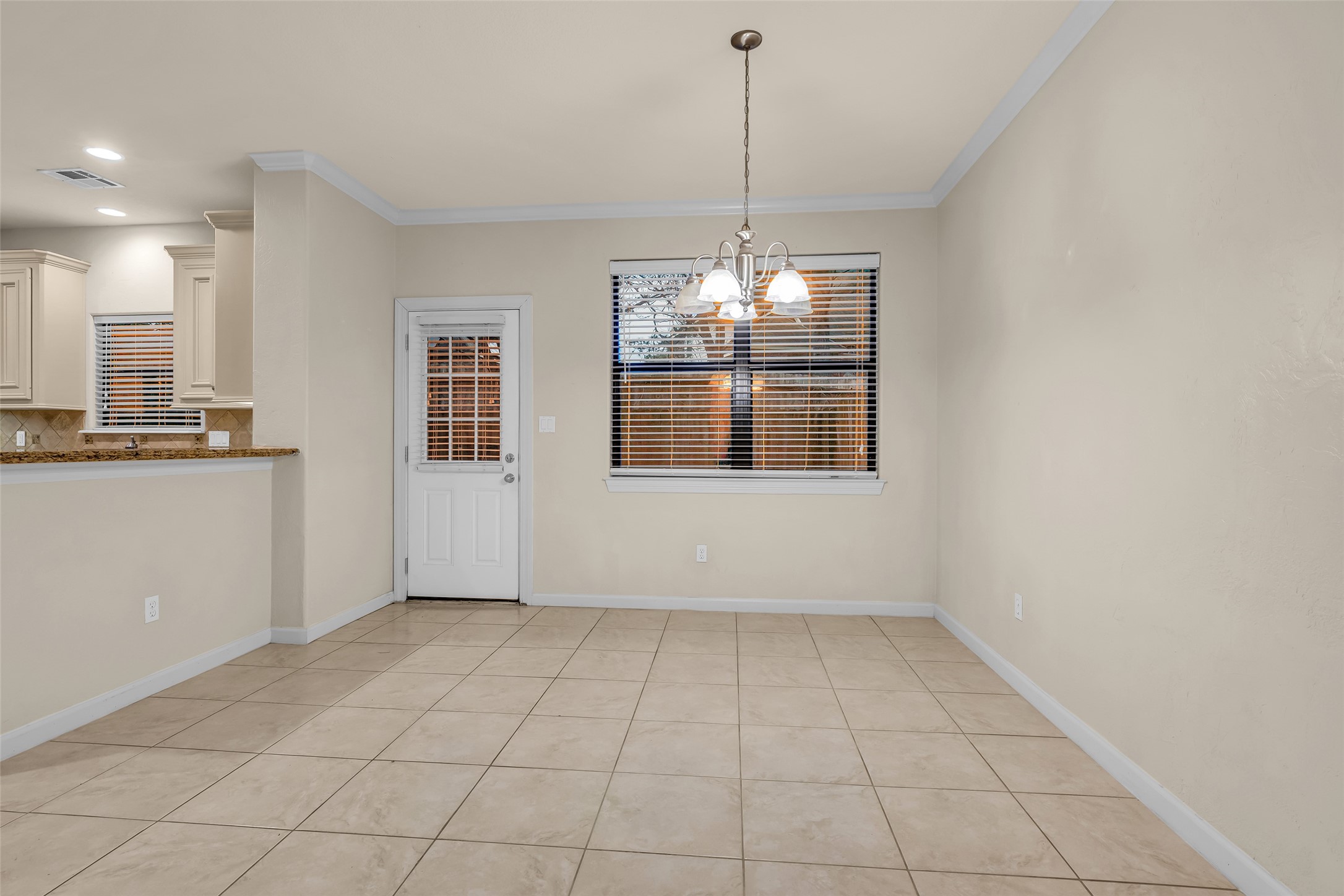 1898 Longmire Road, Unit 5 Conroe, TX 77304 - Photo 24 of 48 This photo shows a bright, open dining area with tiled flooring and a hanging light fixture. It features a partial view of a kitchen with a breakfast bar, light cabinetry, and a door leading outside. The room is well-lit with a window and recessed lighting.