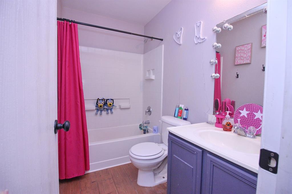 12609 Carpenter Lane Rhome, TX 76078 - Photo 11 of 29 Bathroom featuring wood-finish flooring, a white bathtub with shower, a toilet, a vanity with a white countertop and integrated sink, and a framed mirror