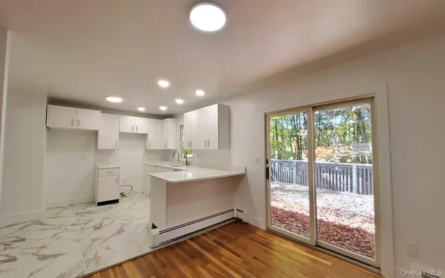 a open kitchen with kitchen island granite countertop a stove a sink and white cabinets with wooden floor