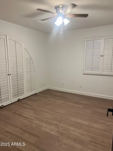 an empty room with wooden floor fan and windows