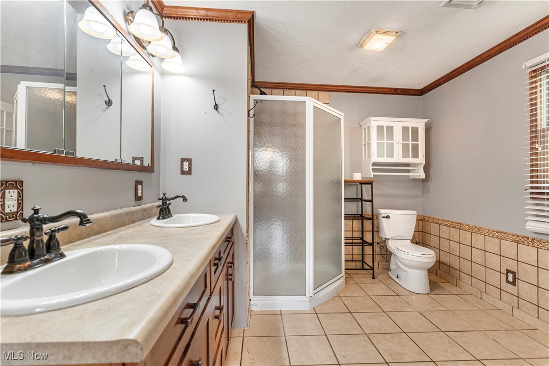 155 Ridgewood Boulevard Belpre, OH 45714 - Photo 44 of 49 Bathroom with a textured ceiling, crown molding, light tile patterned floors, a shower stall, and double vanity