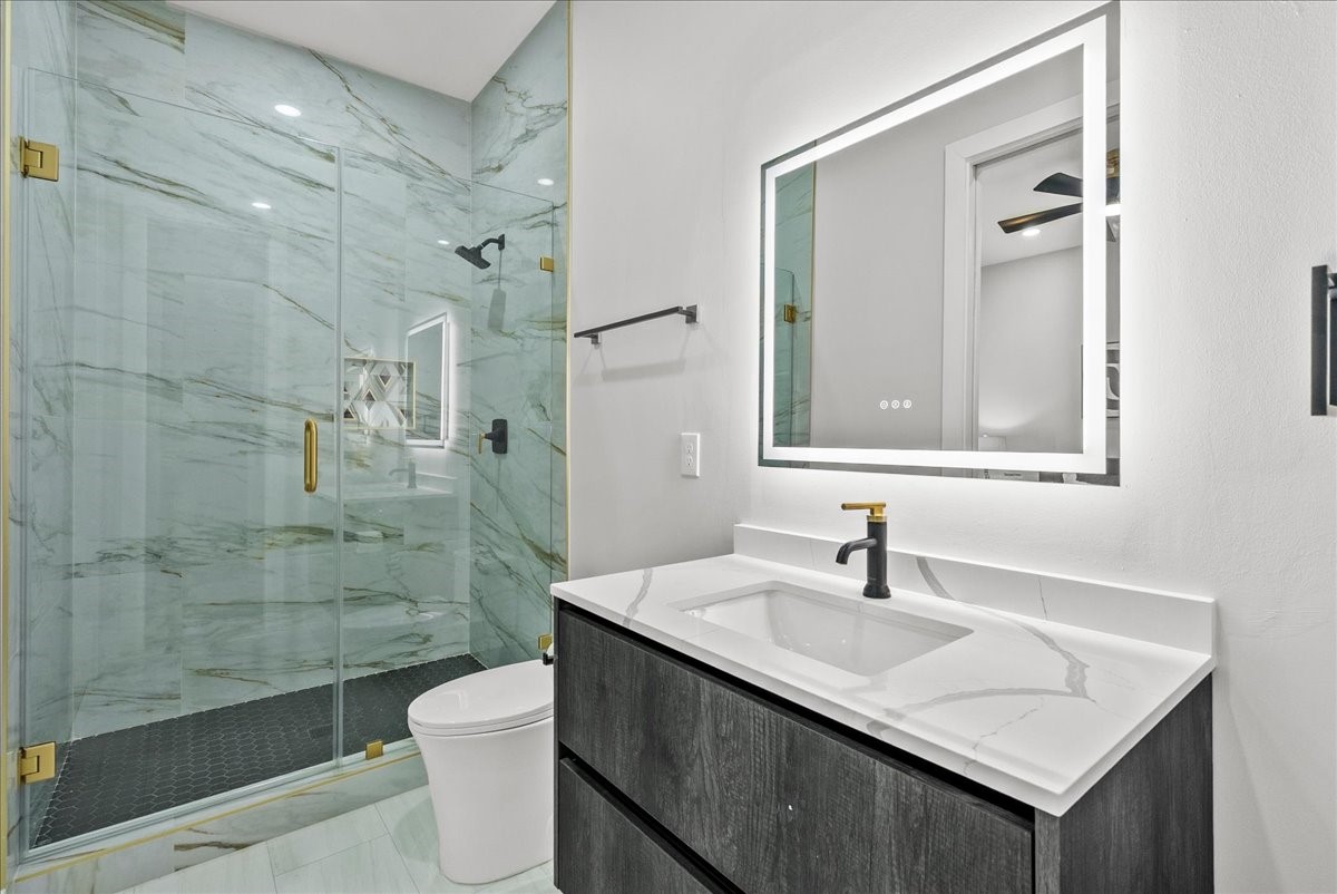 516 Reinerman Street Houston, TX 77007 - Photo 40 of 42 This modern bathroom features a sleek design with a spacious glass-enclosed shower, elegant marble walls, and a stylish vanity with a backlit mirror. The fixtures are contemporary with gold accents, adding a touch of luxury.