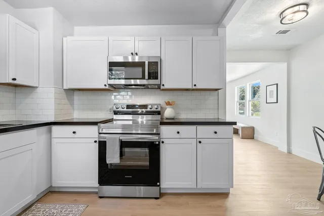 a kitchen with stainless steel appliances granite countertop a stove a microwave and white cabinets
