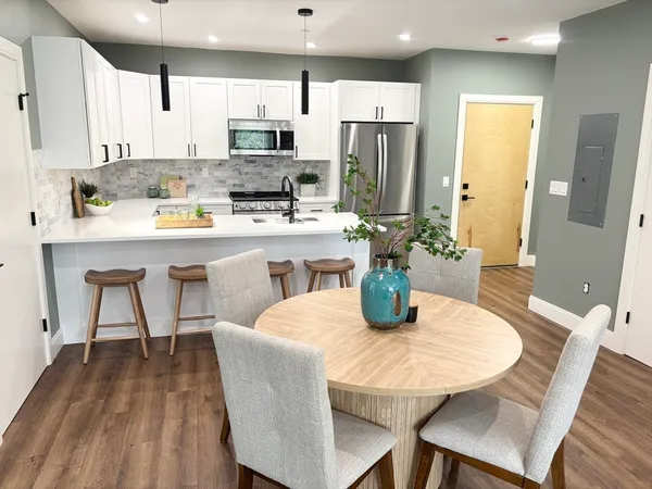 a kitchen with stainless steel appliances granite countertop a dining table chairs refrigerator and microwave