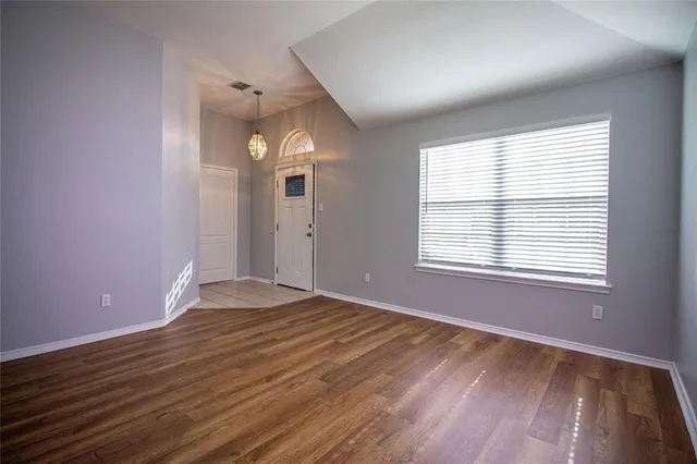 a view of an empty room with wooden floor and a window
