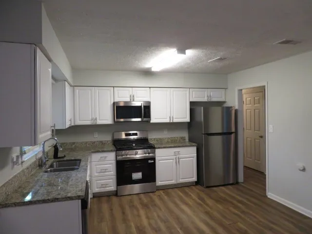 a kitchen with stainless steel appliances granite countertop a refrigerator stove a sink and a granite counter tops with wooden floors