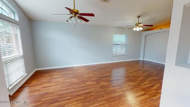 an empty room with wooden floor ceiling fan and windows