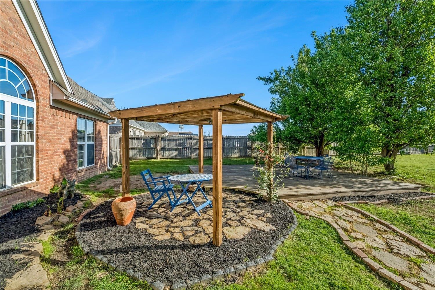 134 Rembert Drive Atoka, TN 38004 - Photo 38 of 38 Expansive backyard featuring a stone paver patio with a wooden pergola, a raised wooden deck, a stone pathway, a brick exterior with arched windows, and mature trees