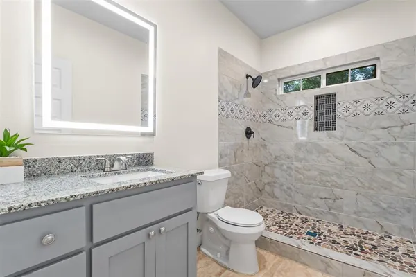 a bathroom with a granite countertop sink a toilet a mirror and shower