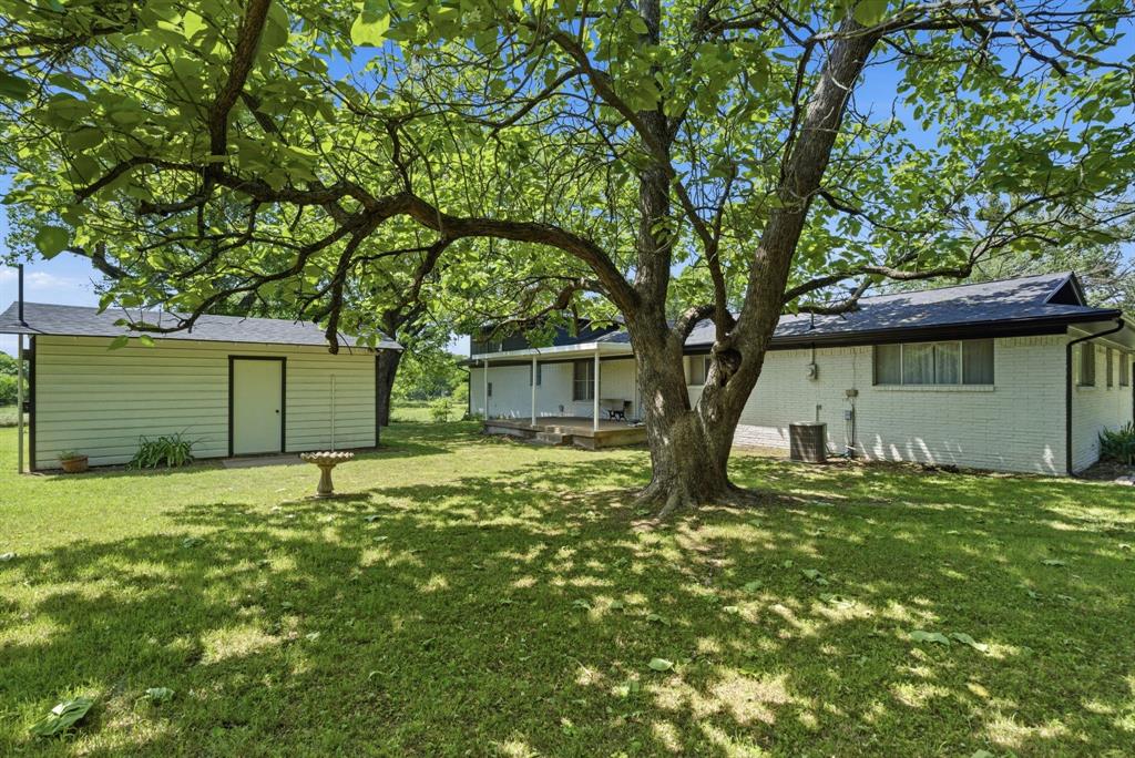 7485 Portwood Road Azle, TX 76020 - Photo 6 of 40 Spacious green lawn with mature shade trees, a detached storage building, and a rear patio
