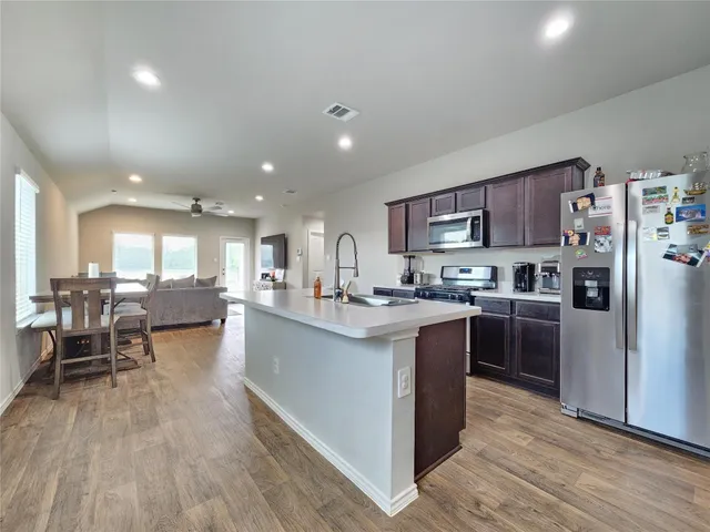 a kitchen with stainless steel appliances granite countertop a refrigerator a stove top oven a sink dishwasher and a dining table with wooden floor