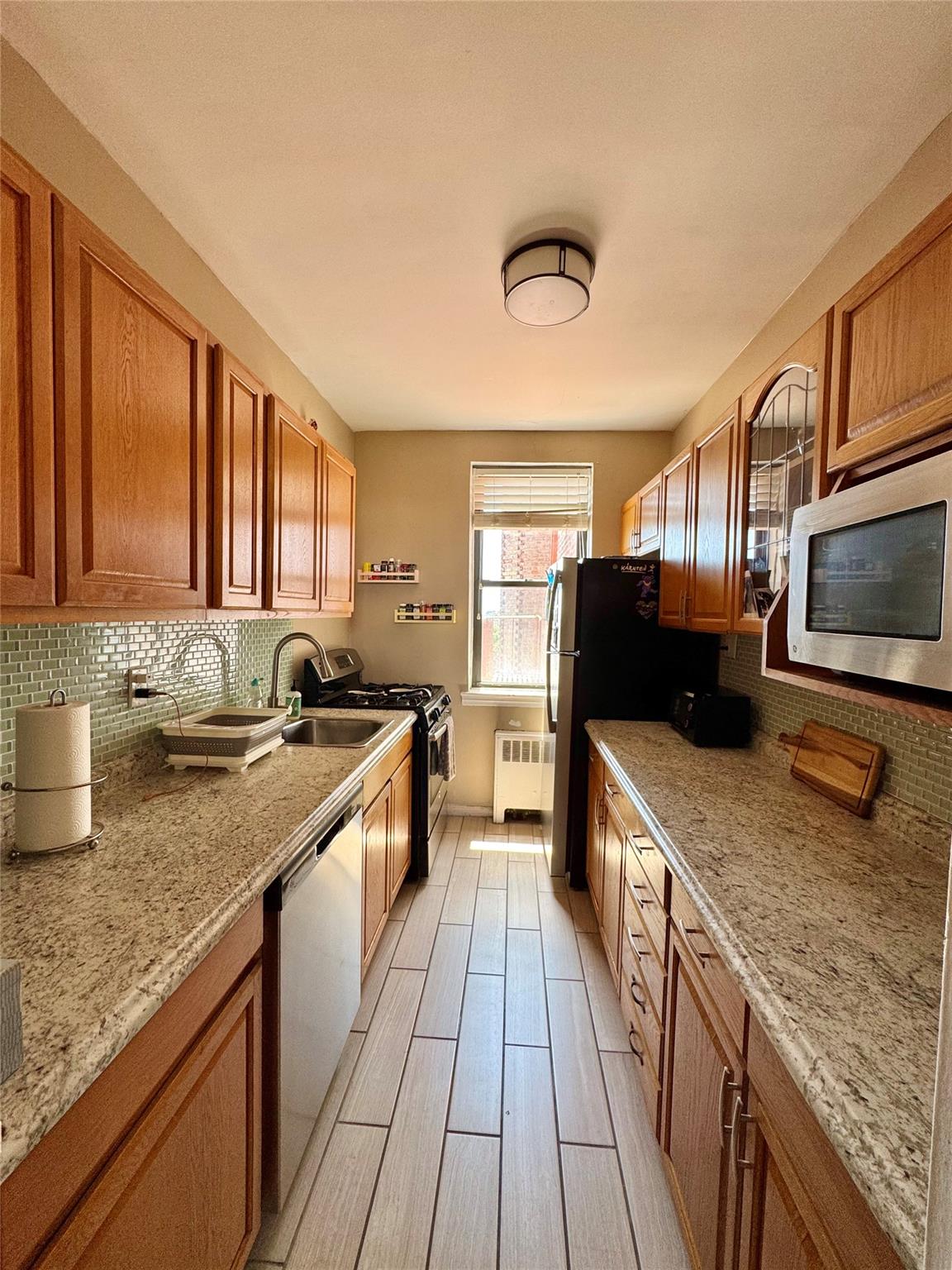 128-11 Newport Avenue, Unit 4A Queens, NY 11694 - Photo 4 of 18 Kitchen with stainless steel appliances, radiator heating unit, tasteful backsplash, and brown cabinetry