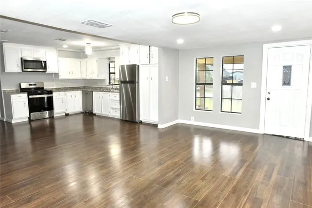 a view of kitchen with stainless steel appliances granite countertop a stove top oven a refrigerator a sink and dishwasher with wooden floor