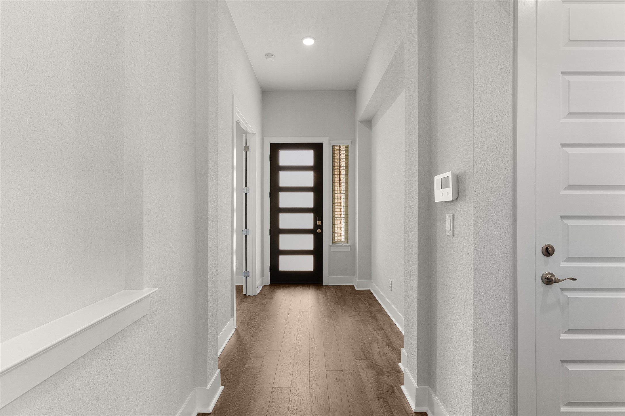 1129 Pansy Trail Georgetown, TX 78628 - Photo 4 of 29 Inviting hallway featuring wood-finish flooring, recessed ceiling lighting, a modern dark-paneled door with frosted glass inserts, and a sidelight window with blinds