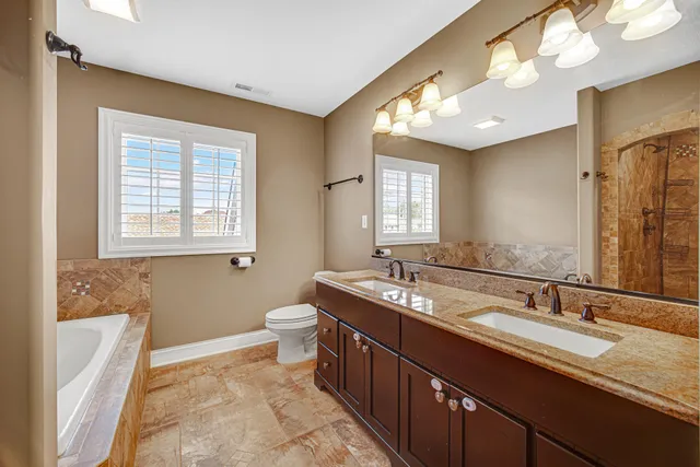 a bathroom with a granite countertop double vanity sink a mirror and a bathtub