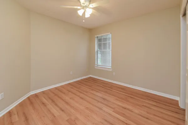 an empty room with wooden floor fan and windows