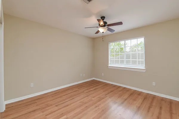 an empty room with wooden floor fan and windows