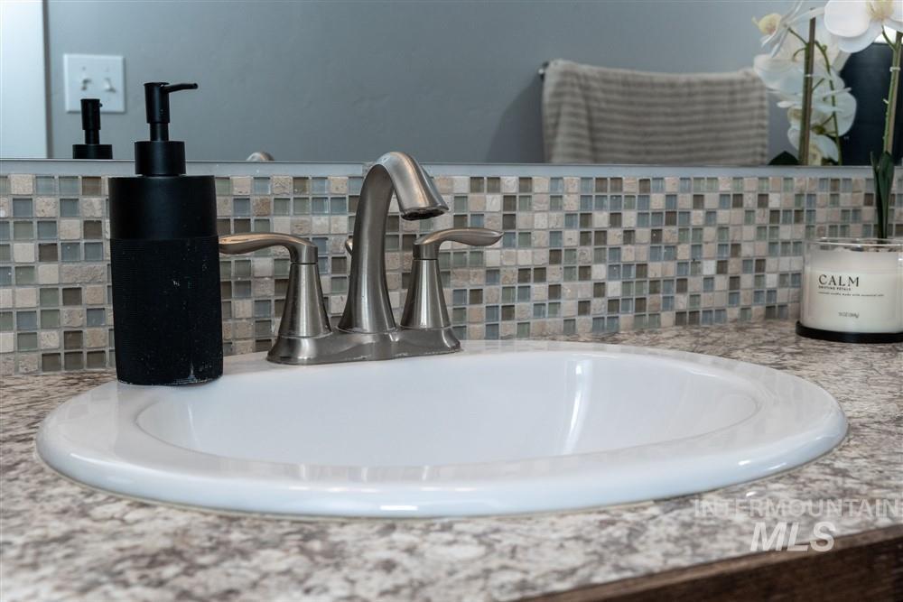 2160 East Ridgeview Avenue Payette, ID 83661 - Photo 16 of 32 Built-in vanity featuring a white oval sink, brushed nickel faucet, speckled countertop, and a mosaic tile backsplash