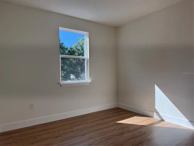 a view of an empty room with wooden floor and a window