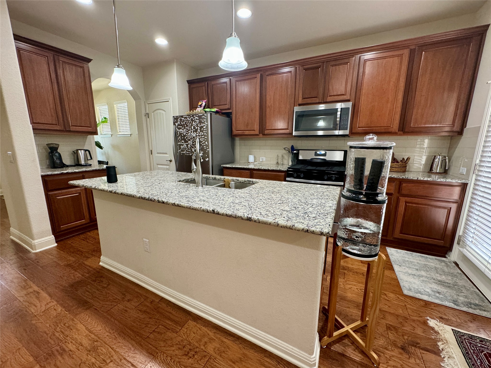 5904 Baythorne Drive Austin, TX 78747 - Photo 8 of 24 Kitchen with stainless steel appliances, dark wood-style floors, decorative light fixtures, an island with sink, and light stone countertops