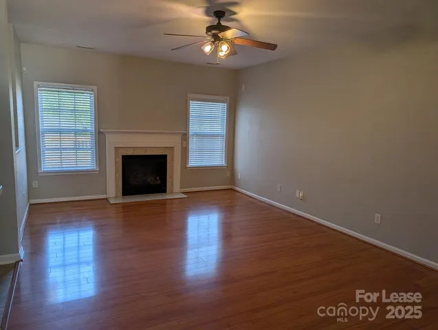 a view of an empty room with wooden floor fireplace and a window