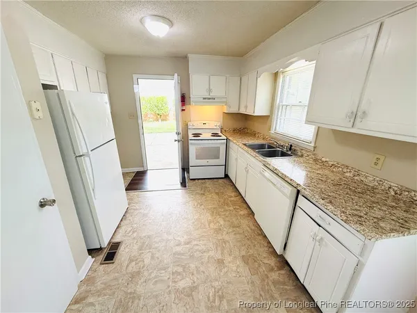 a kitchen with granite countertop a refrigerator a sink a stove a washer dryer and white cabinets