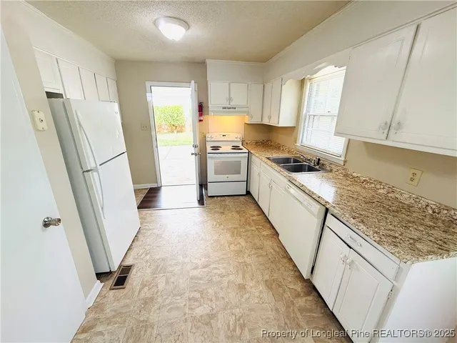 a kitchen with granite countertop a refrigerator a sink a stove a washer dryer and white cabinets