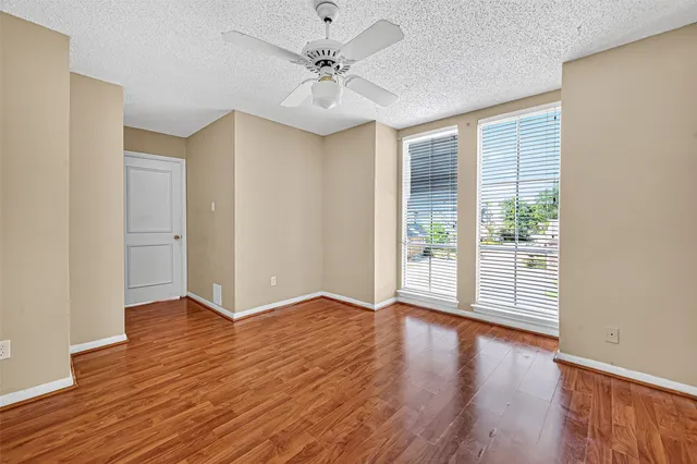 an empty room with wooden floor chandelier fan and windows