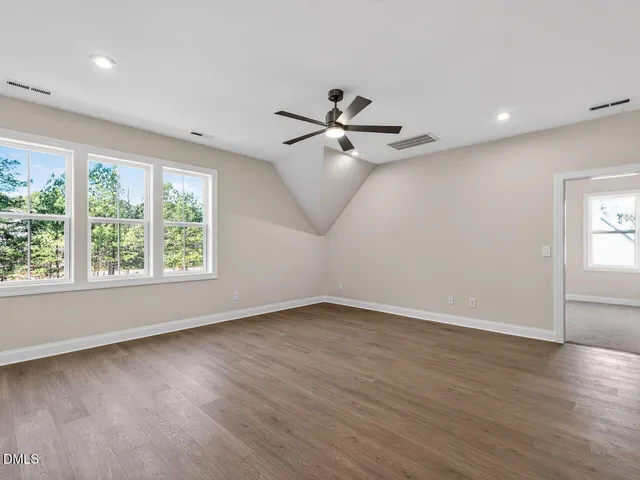 an empty room with wooden floor fan and windows