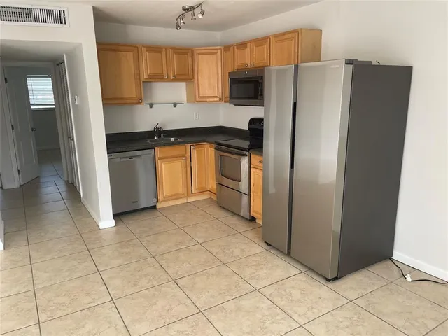 a view of a refrigerator in kitchen and an empty room in wooden floor
