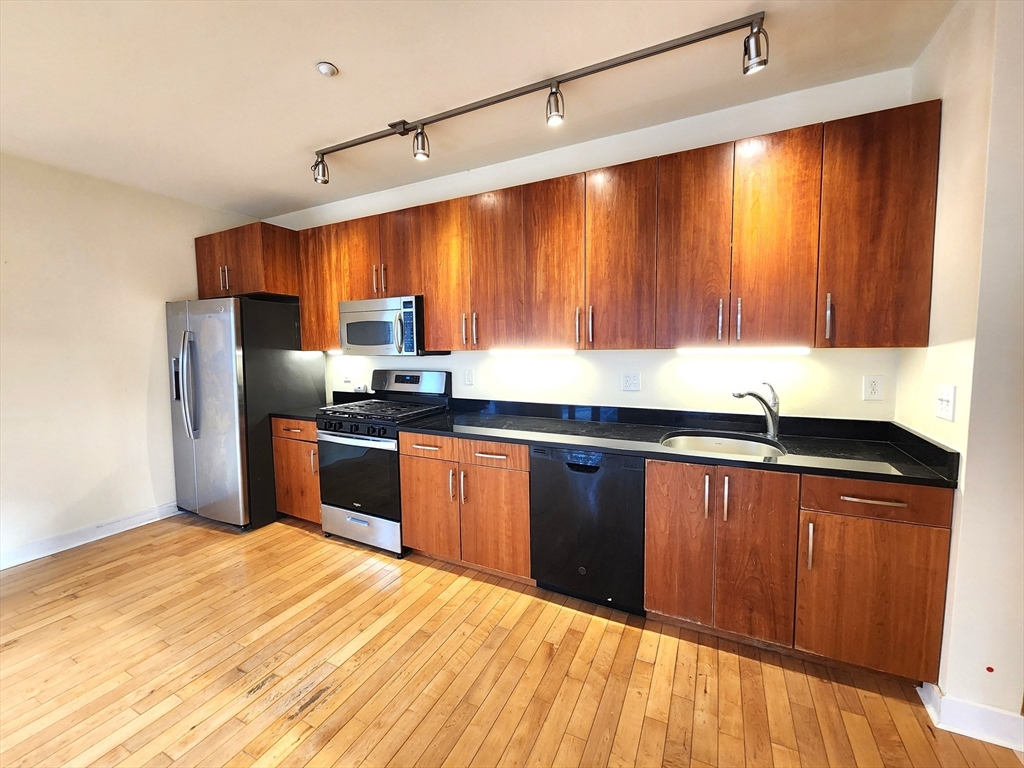 24 Bay State Road, Unit 11 Cambridge, MA 02138 - Photo 9 of 26 a kitchen with stainless steel appliances granite countertop a refrigerator a sink dishwasher and wooden cabinets with wooden floor