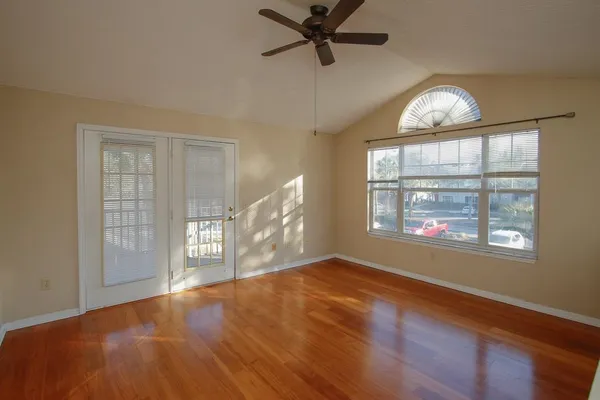 an empty room with wooden floor chandelier fan and windows