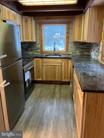 a kitchen with granite countertop a refrigerator a sink dishwasher and wooden cabinets with wooden floor