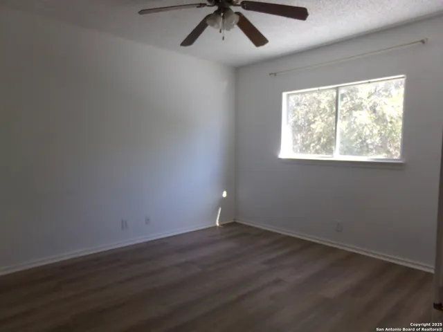 an empty room with wooden floor chandelier fan and windows