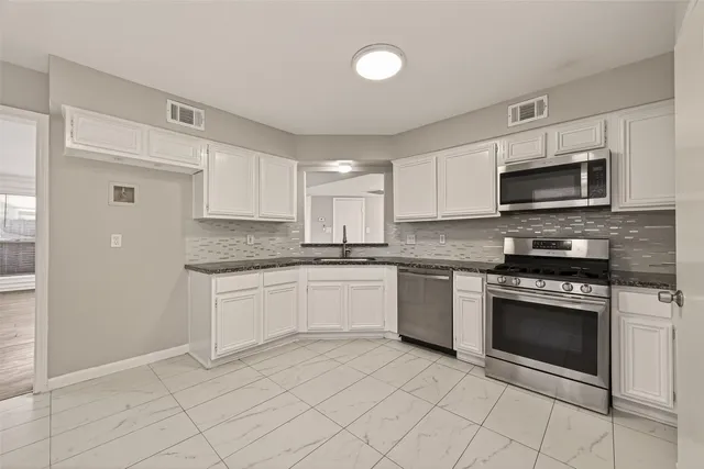 a kitchen with granite countertop white cabinets stainless steel appliances and a counter space