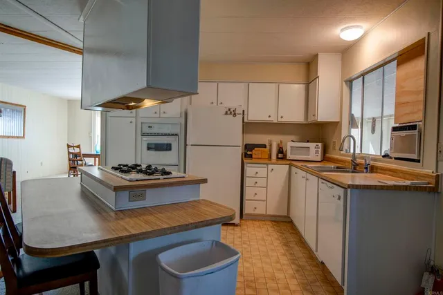 a kitchen with stainless steel appliances a stove a refrigerator a sink and white cabinets with wooden chairs