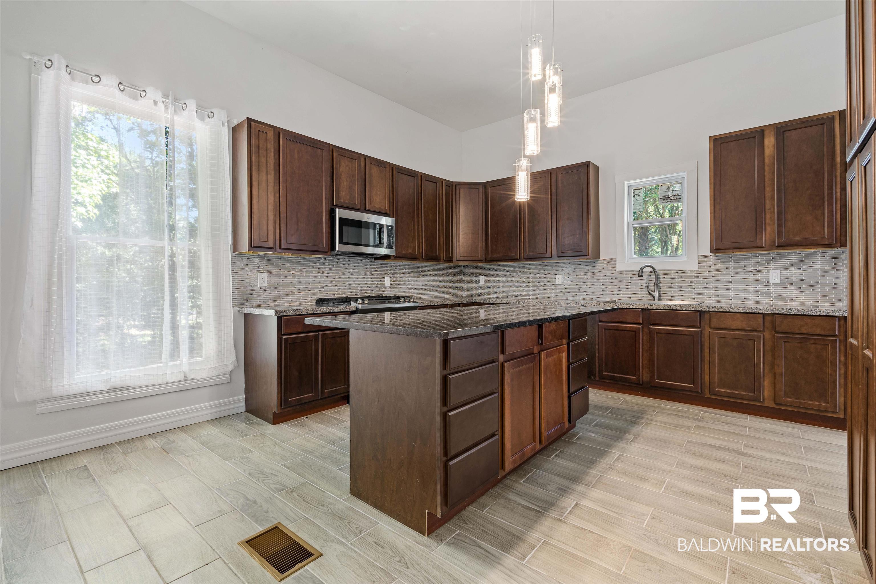 407 East 2nd Street Bay Minette, AL 36507 - Photo 8 of 40 Kitchen with pendant lighting, wood tiled floors, dark stone countertops, stainless steel microwave, and backsplash