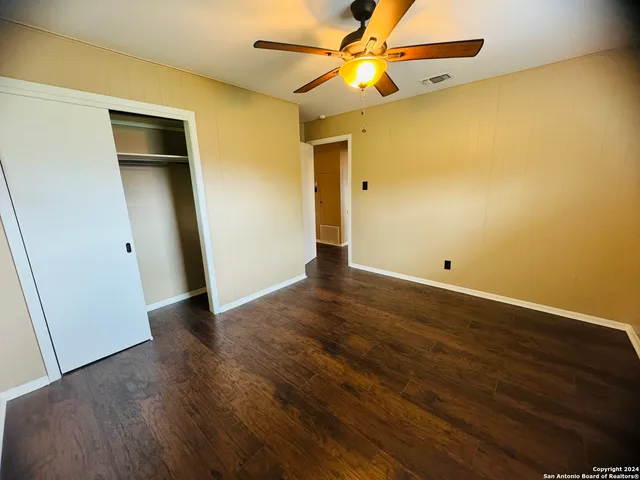 an empty room with wooden floor and fan