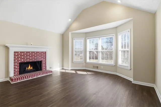 a view of an empty room with wooden floor fireplace and a window