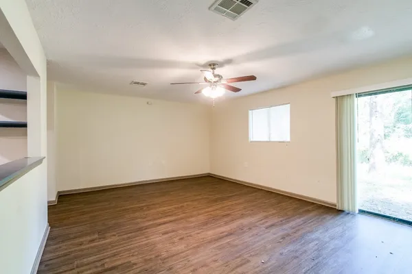 an empty room with wooden floor chandelier fan and windows