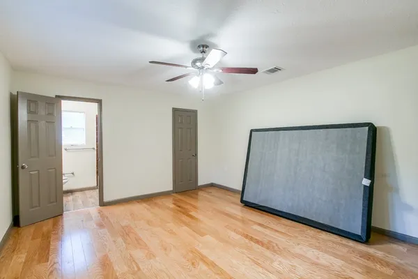 a view of an empty room with wooden floor and a ceiling fan
