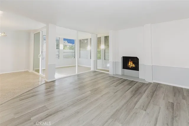 an empty room with wooden floor fire place and windows
