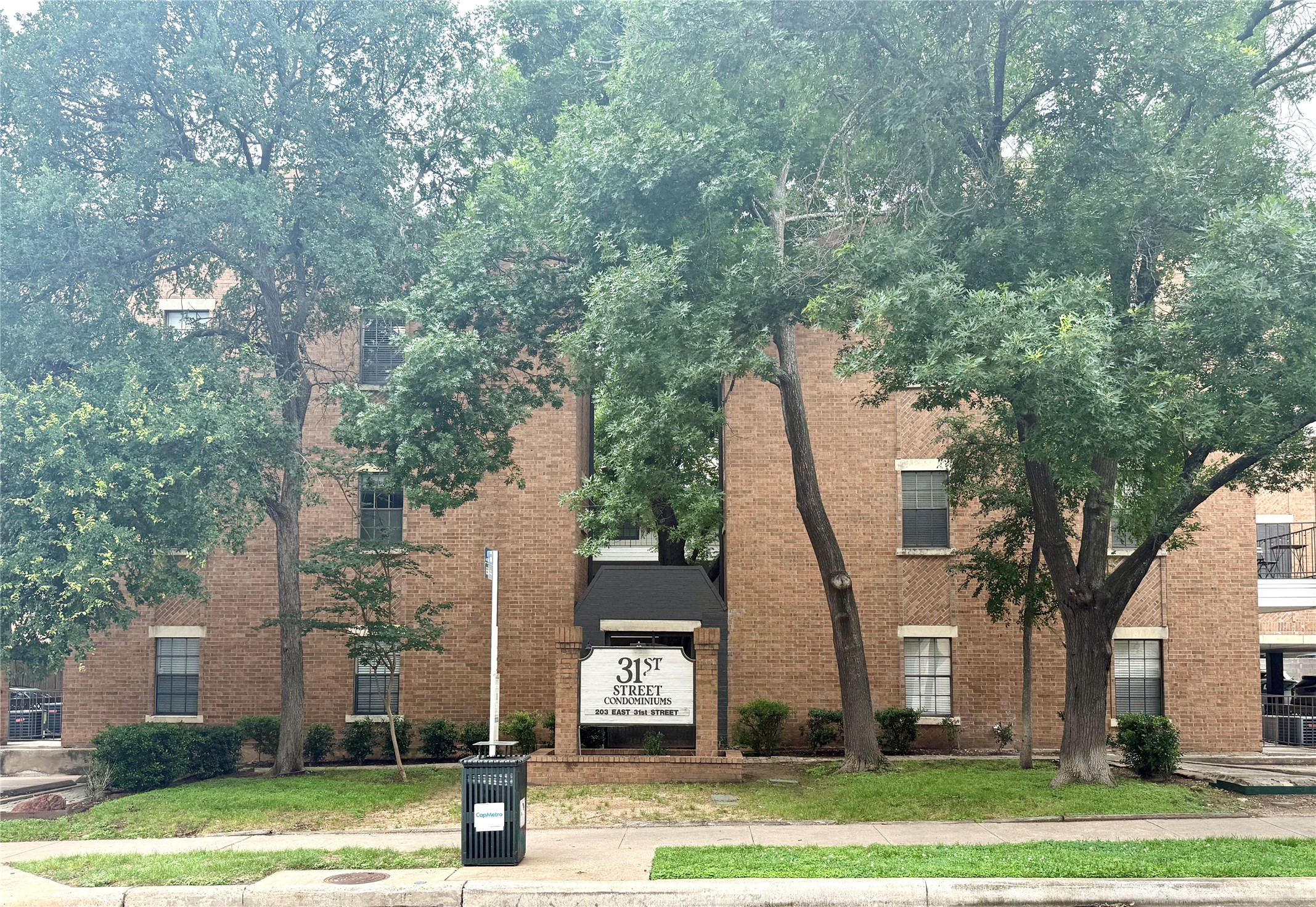 203 East 31st Street, Unit 101 Austin, TX 78705 - Photo 1 of 24 Brick exterior building with multiple windows, framed by mature trees