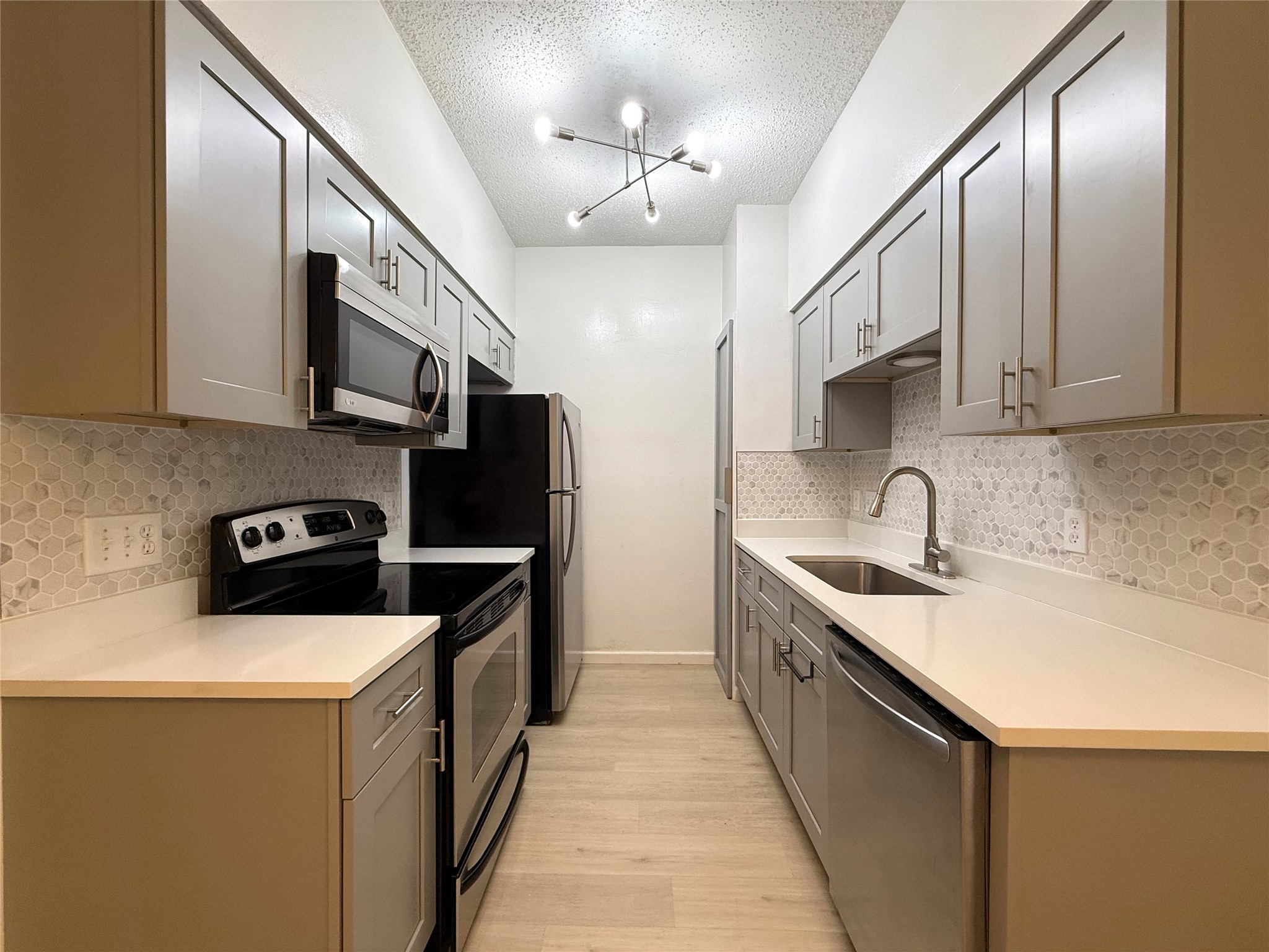 203 East 31st Street, Unit 101 Austin, TX 78705 - Photo 11 of 24 Galley kitchen featuring light gray cabinetry with brushed nickel hardware, white countertops, stainless steel appliances, and a hexagonal tile backsplash