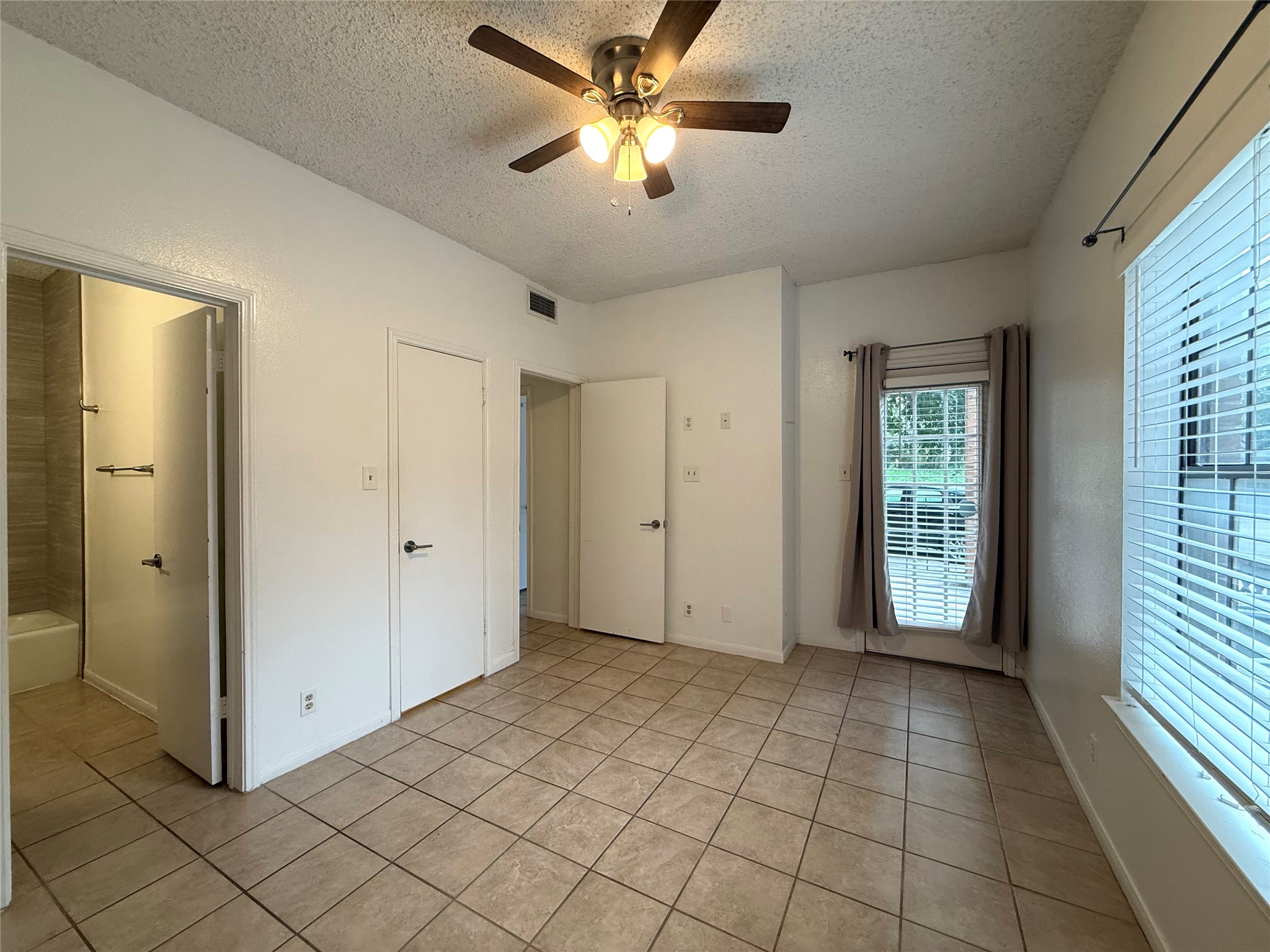 203 East 31st Street, Unit 101 Austin, TX 78705 - Photo 18 of 24 Spacious room featuring tile flooring, a window with blinds and drapes, a ceiling fan with integrated lighting, and multiple interior doors