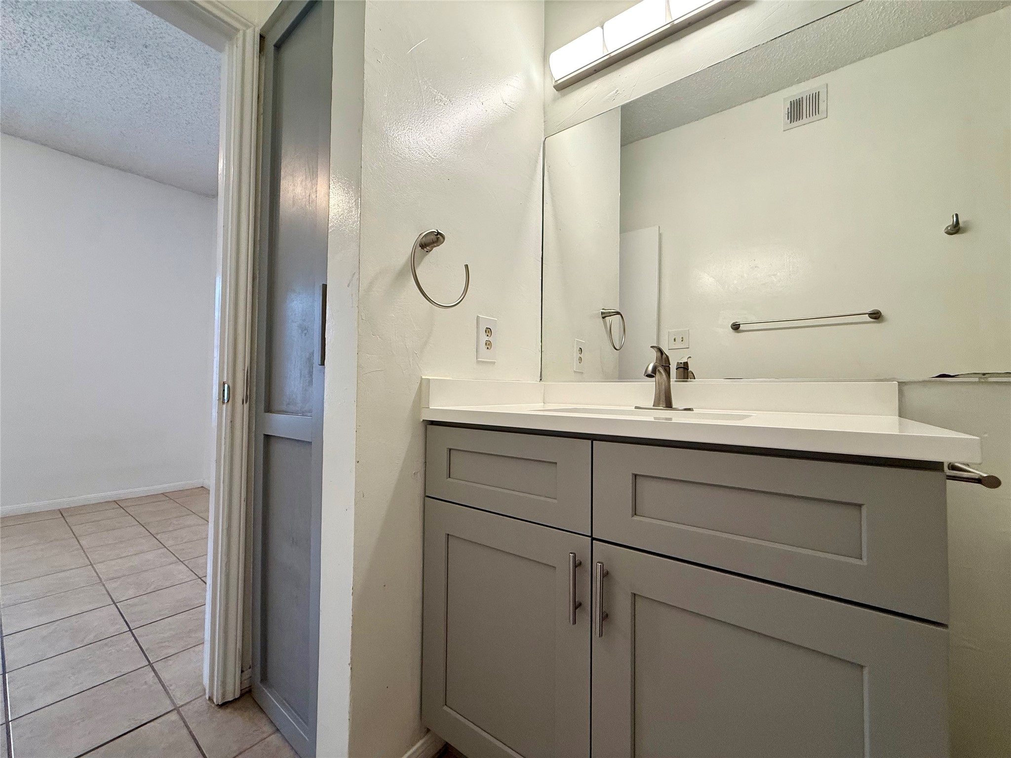 203 East 31st Street, Unit 101 Austin, TX 78705 - Photo 20 of 24 Bathroom vanity featuring gray shaker-style cabinetry, a white countertop with integrated sink, and a large wall-mounted mirror