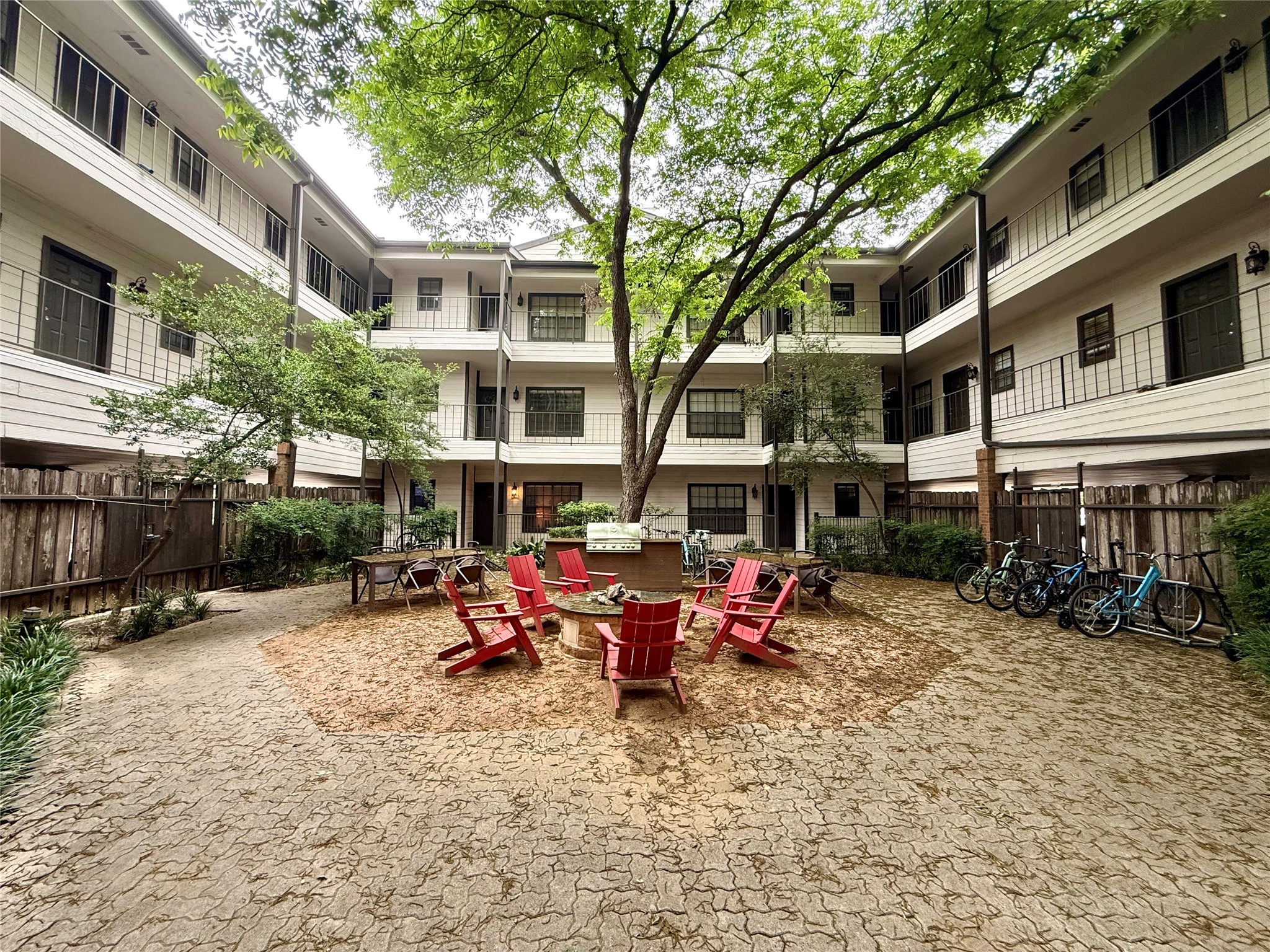 203 East 31st Street, Unit 101 Austin, TX 78705 - Photo 24 of 24 Courtyard featuring a large central tree, paver stone hardscaping, perimeter fencing, and multi-level building exteriors with balconies and walkways