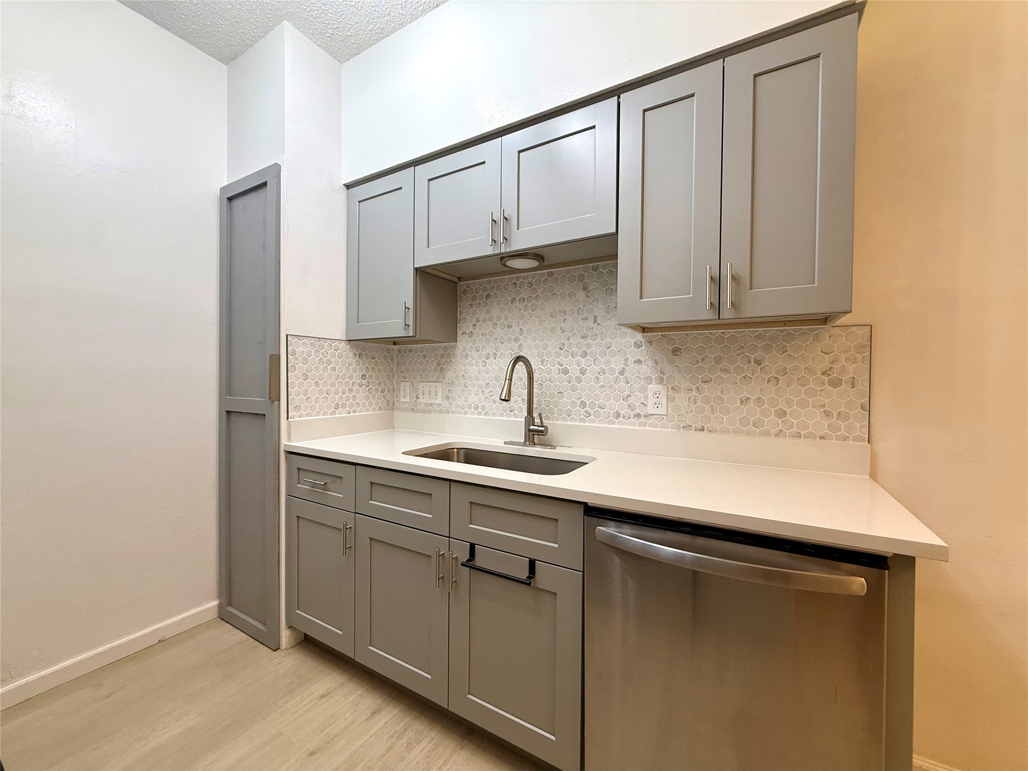 203 East 31st Street, Unit 101 Austin, TX 78705 - Photo 9 of 24 Kitchenette featuring light gray shaker-style cabinetry, a white countertop, stainless steel sink with a gooseneck faucet, a mosaic tile backsplash, and wood-finish flooring