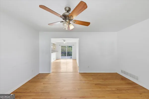 a view of an empty room with wooden floor and a chandelier fan