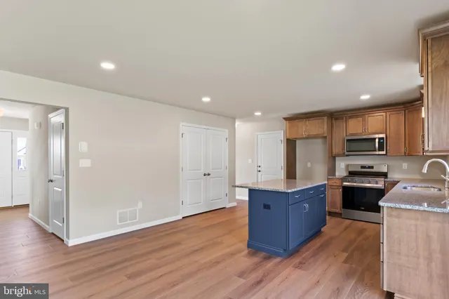 a kitchen with stainless steel appliances granite countertop a refrigerator a stove top oven a sink with wooden floors and cabinets